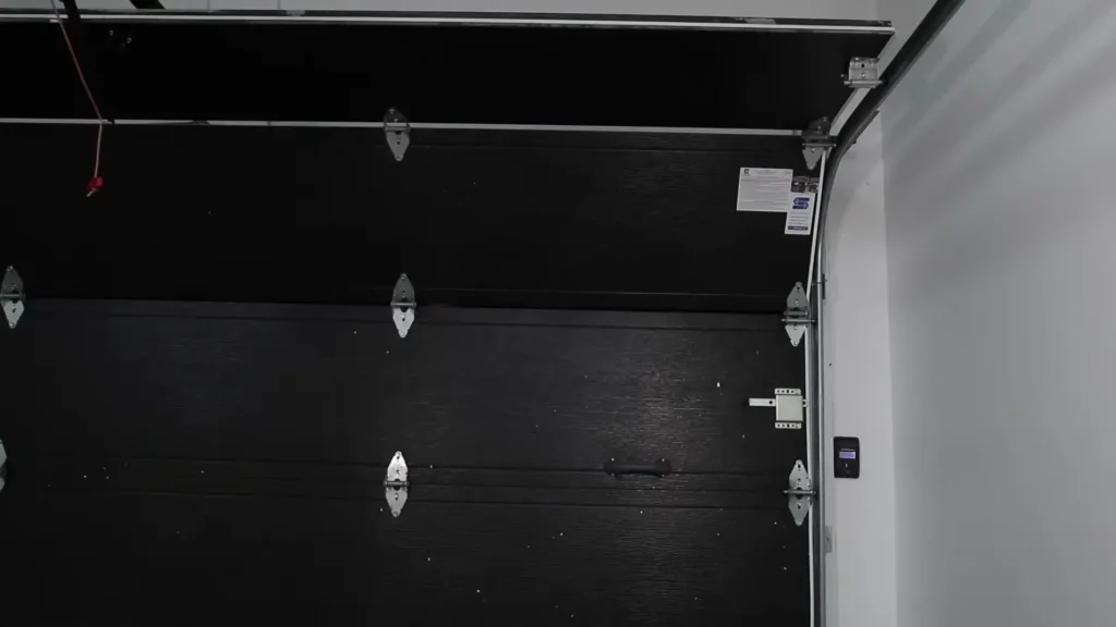 Close-up of a black garage door highlighting hinges and tracks, showcasing the importance of regular maintenance for smooth operation. Call Unhinged for professional garage door and gate services.