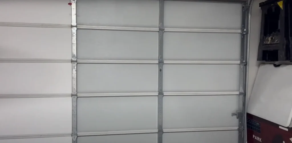A white garage door with metal framing, prepared for potential insulation installation to enhance energy efficiency and temperature control.