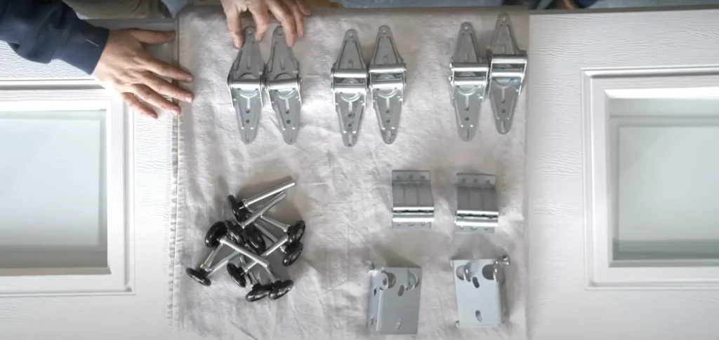Various components for an overhead door installation laid out neatly on a white cloth, including rollers, hinges, and brackets.