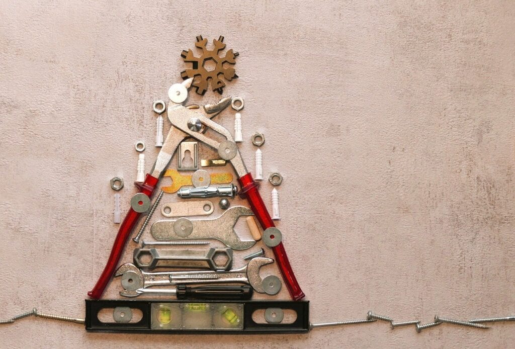 A creative arrangement of tools like wrenches, screwdrivers, nuts, bolts, and screws, forming the shape of a Christmas tree, topped with a snowflake-shaped ornament.