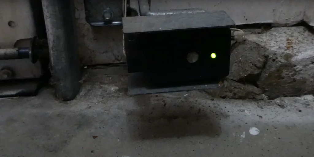 Close-up of a safety sensor with a green light indicator installed near the bottom of a commercial garage door track.